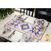 Table runner with geometric design with white and purple lavender and bee themed fabrics on table set with matching napkins.
