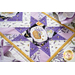 Table runner with geometric design with white and purple lavender and bee themed fabrics on table set with matching napkins.