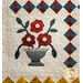 A quilt featuring a blue vase with three colorful flowers and a patterned border in red and yellow.