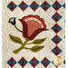 A detailed quilt featuring a large red flower and green leaves, surrounded by blue and red diamond patterns.