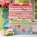 A stacked arrangement of colorful fabric swatches featuring floral and polka dot patterns in shades of pink, red, green, and blue, alongside spools of green and beige thread.