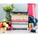 A stack of neatly arranged colorful fabric rolls sits on a table next to a bouquet of tulips and spools of thread. In the background, there is a vase with green leaves and a large blue flower.