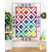 A large white quilt with colorful diamond blocks hung on a white wall.