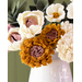 Flowers made of fabric being displayed in a white vase on small wood table.