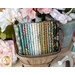 A wooden basket filled with neatly folded fabrics in various colors and patterns, surrounded by pastel-colored flowers and sewing supplies.