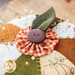 An orange, white, and green pin cushion with a small button topper on a wood table