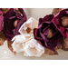 Close up of flowers on wreath of foliage and flowers toped with a gold ribbon hanging from wall.