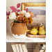 Gold and white paper flowers and red paper leaves with stems in a clay vase next to pears.