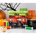 A stack of vibrant Halloween-themed fabric bundles in various colors, including green, orange, black, and white, is displayed alongside spools of thread in green, orange, and red. In the background, there are decorative pumpkins and jars filled with candy.