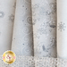 A collection of rolled gray and white fabrics featuring various winter-themed patterns, including swirls, snowflakes, and floral designs. A textured ribbon is partially visible at the bottom of the image.