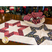 Table runner with 3 hollow star design made of red, black, and green winter theme printed fabric on cream.