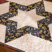 Quilted tabletop decoration featuring a star pattern with black and cream fabrics, accented by holly leaves.