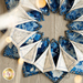 A circular arrangement of fabric pieces in blue and white floral patterns, with some sections oriented outward to create a fan-like effect. The background features a light wood texture.