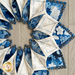 A circular arrangement of fabric pieces in blue and white floral patterns, with a mix of bright and muted tones, set against a light wooden background.