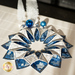 A decorative blue and white fabric wreath made of layered triangular shapes, adorned with blue ornaments and small white trees.