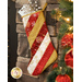 A festive Christmas stocking with diagonal red, white, and gold stripes adorned with snowflake patterns, hanging by a stone fireplace, surrounded by holiday decorations.