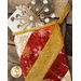 A decorative stocking in red, gold, and white fabric with snowflake patterns is hanging against a stone surface. It is filled with a folded card and topped with a sparkly, star-shaped decoration made of crystals.