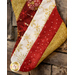 A decorative Christmas stocking made of red, white, and gold fabric with festive patterns, hanging against a stone wall.