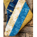 A decorative Christmas stocking with a patchwork design featuring blue and gold fabrics, embellished with snowflakes and patterns, hangs against a stone wall.