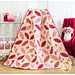 Completed quilt draped in front of a white wall with a chair draped with a red blanket and white shelf with decorations in the background
