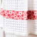 Close up of the bottom of the hanging towel showing a waffle patterned white towel with a pink fabric stripe featuring tiny red and white flowers on it.