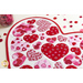 Close up angled shot of heart table topper with different sized hearts in red and pink on a white background on a white table with a jar of red and pink buttons and buttons scattered all over the table