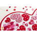 Close up angled shot of heart table topper with different sized hearts in red and pink on a white background on a white table with red and pink buttons scattered all over the table
