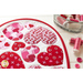 Close up angled shot of heart table topper with different sized hearts in red and pink on a white background on a white table with a dish of red and pink spools of thread and buttons scattered on the table