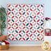 Photo of a red, white and blue quilt hanging vertically on a light blue paneled wall with patriotic decor and a houseplant on either side.