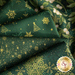 A close-up of folded fabric featuring a green background with gold patterns, including Christmas trees, snowflakes, and holly leaves.