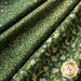 A close-up of folded fabric featuring a green background with gold patterns, including berries, leaves, and speckles