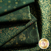 A collection of folded green fabrics with various patterns, including floral designs and festive motifs in gold and red. The fabrics are layered together, showcasing their intricate prints.