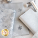 A collection of silver and grey fabrics with decorative designs, including snowflakes and intricate patterns, along with spools of silver thread. A logo for Shabby Fabrics is displayed in the corner.