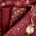 A collection of burgundy fabric pieces adorned with golden snowflake and swirl patterns, accompanied by a gold ribbon.