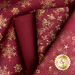 A collection of fabrics in rich red hues featuring gold patterns, including snowflakes, ornate designs, and shimmering star accents, arranged in a visually appealing display.