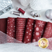 Close up of dark red fabric with metallic silver winter motifs layered atop one another on a white countertop with red and silver spools of thread and winter decorations with silver baubles laying next to them and mesh silver ribbon laying on top