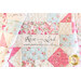 close up image with an overlapped quilt made of rectangular, diamond, and triangular blocks in pink, blue, and cream cream floral fabrics with a small panel with the words 