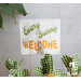 A small fabric flag with the text Every Bunny Welcome in green and orange, placed among green and white checkered decorations.