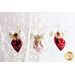 Three decorative fabric angels are hanging on a string against a blurred background of twinkling lights. The angels are made from red, pink, and cream fabric with bows at the top and embellishments.