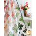 A colorful quilt drapes against a white wall, with a vase of tulips and fabric bundles nearby.