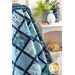 A vibrant blue quilt drapes over a shelf with coastal decor, including shells and greenery.