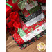 Close up of a festive tree skirt made with red, green, black, and white fabric strips under a decorated Christmas tree with wrapped gifts to one side.