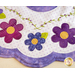 A close-up of a quilted fabric featuring a scalloped edge with colorful flower motifs in purple, blue, and pink, each with yellow centers. The background has polka dots and green vine details.