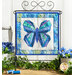 The completed Foundation Paper Piecing Kit - June, a beautiful butterfly colored in blue, teal, and indigo fabrics, displayed on a craft stand and staged with a coordinating décor.