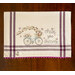 A decorative tablecloth featuring a blue bicycle adorned with flowers and the text Chase your dreams. The cloth has purple stripes and a pink scalloped edge.