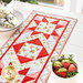 close up of one end of the table runner showing fabric and design detail with a stack of two plates with matching napkins on one side and a bowl of fabric strawberries on the other in the foreground.