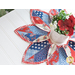 Leaf shaped table topper with central opening containing a floral centerpiece. Topper is made of red white and blue patriotic fabrics.