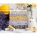 A stack of fabric bundles in various shades of yellow, grey, and white is displayed, accompanied by spools of thread in similar colors. There is a decorative honey jar and a bouquet of flowers in the background, along with lavender sprigs.