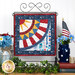 Photo of finished patriotic quilt square on a craft hanger sitting on a brown countertop with a white paneled wall in the background and patriotic decor and plants on either side.