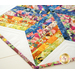 A vibrant patchwork quilt featuring brightly colored strips of fabric arranged in a geometric pattern, surrounded by white borders. The fabrics are adorned with various floral designs, creating a cheerful and colorful visual.